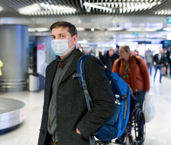 man standing at airport baggage claim with mask on
