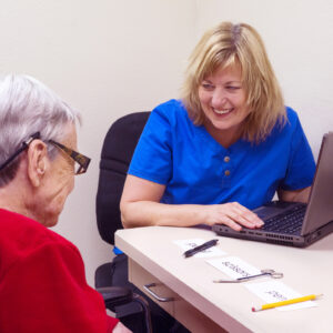 Blond Caucasian speech language pathologist laughs with a senior aged female aphasic patient during speech therapy session targeting visual comprehension skills. Patient realized she incorrectly matched objects to a field of three single written words.