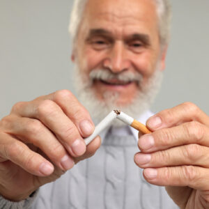 Stop smoking concept. Senior man breaking cigarette on light grey background, selective focus